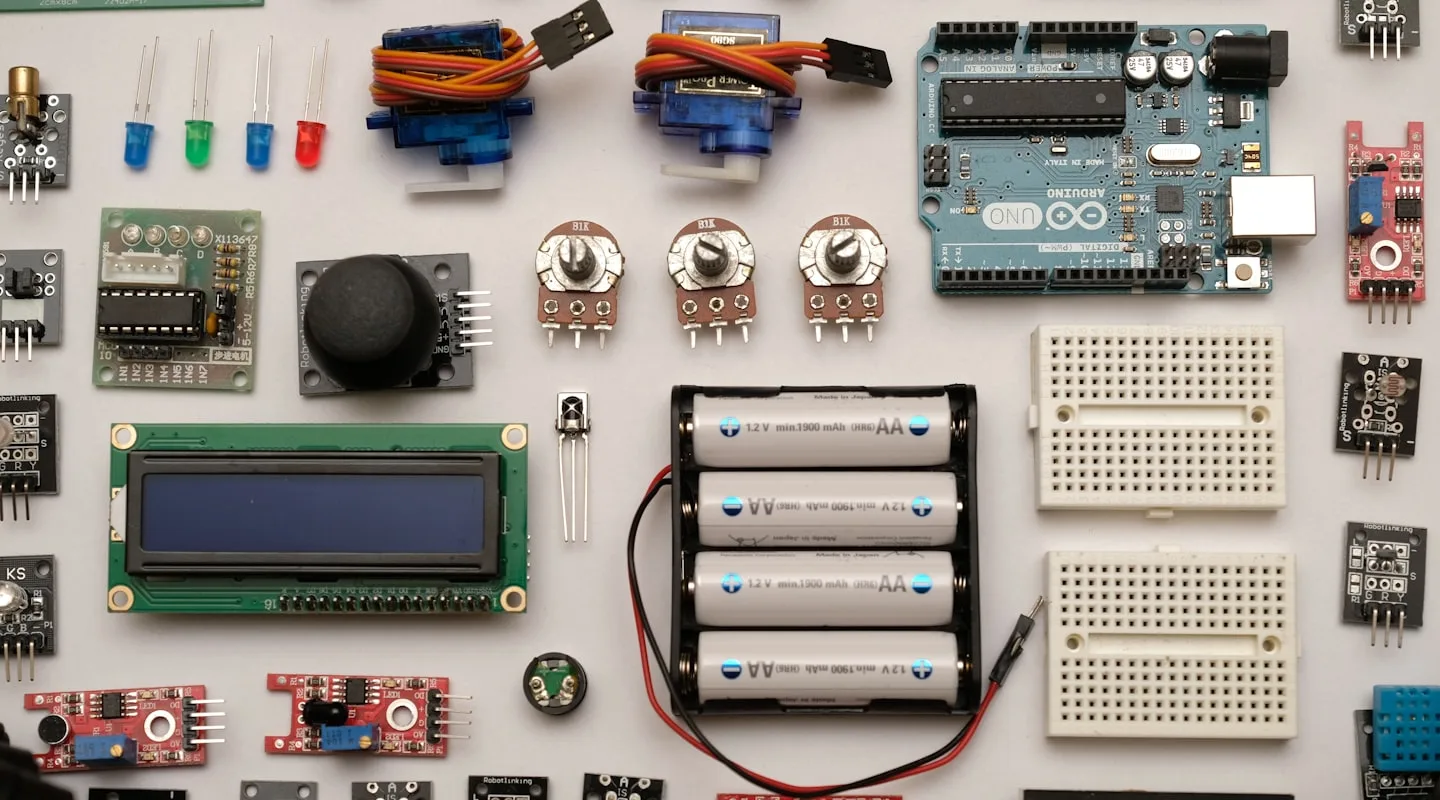 Flat lay of robotics components — Arduino board, sensors, LEDs, potentiometers, breadboard, and battery pack